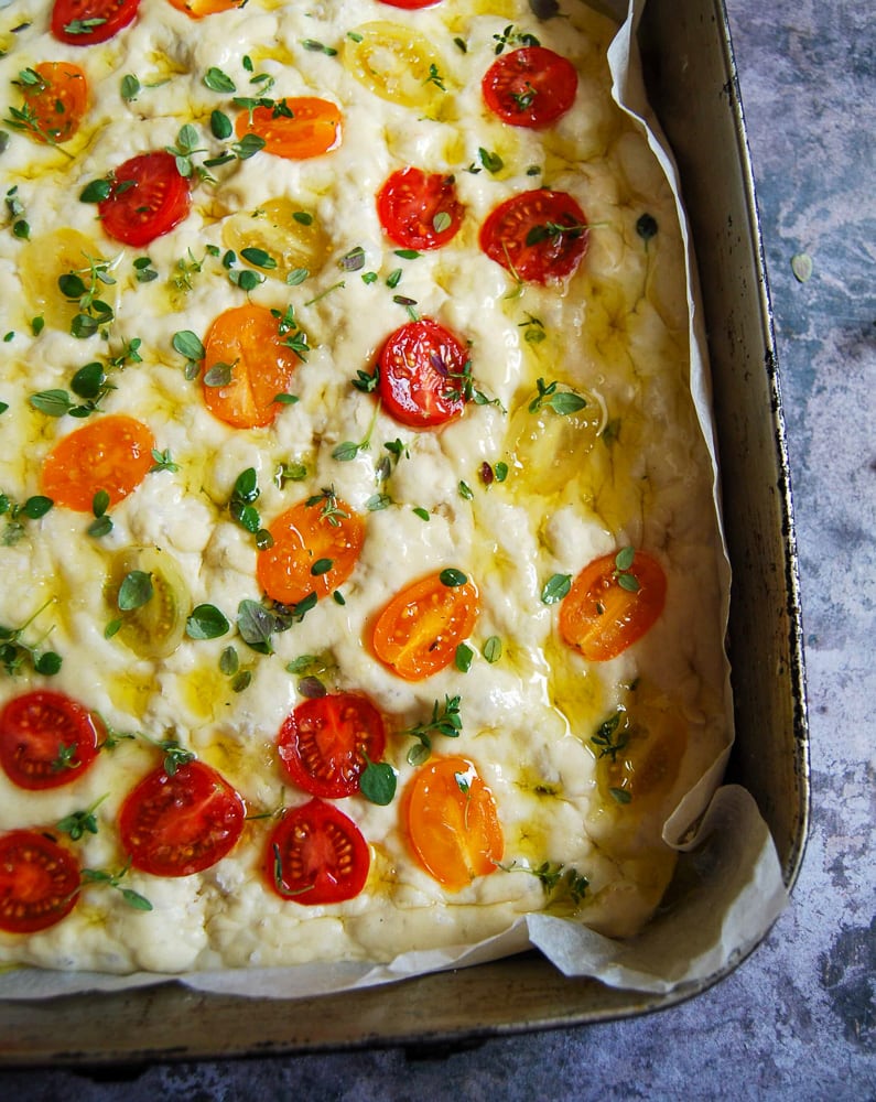 a tray of unbaked Focaccia bread dough with fresh cherry tomatoes and thyme