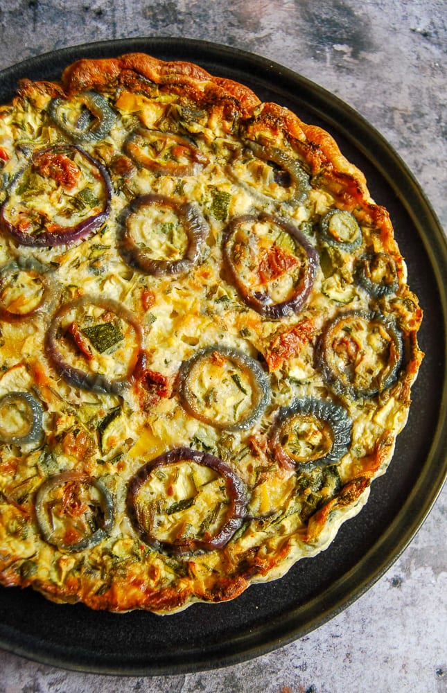 A Flat Lay close up photo of a crustless quiche with red onion rings on the top in an attractive pattern.