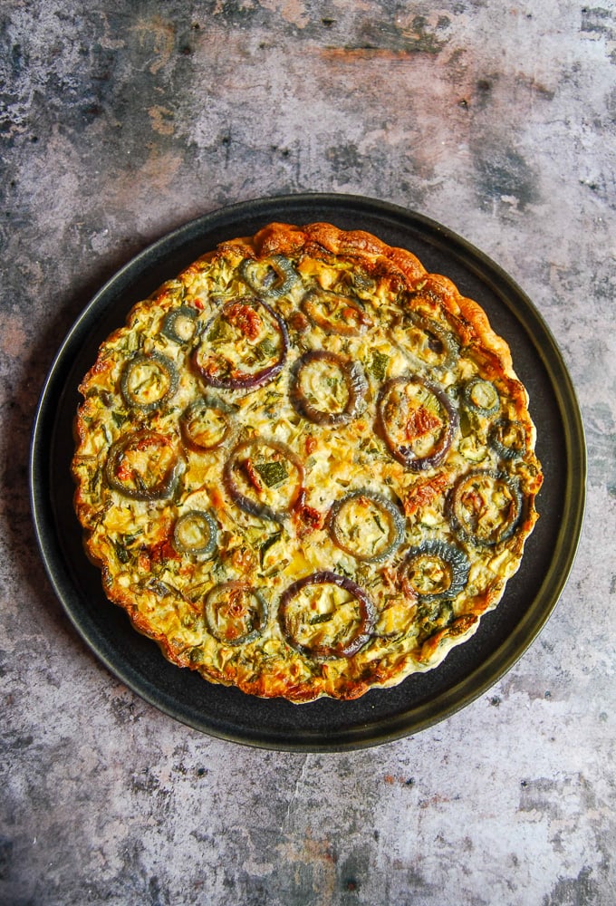 A flatlay photo of a crustless quiche on a black plate. 