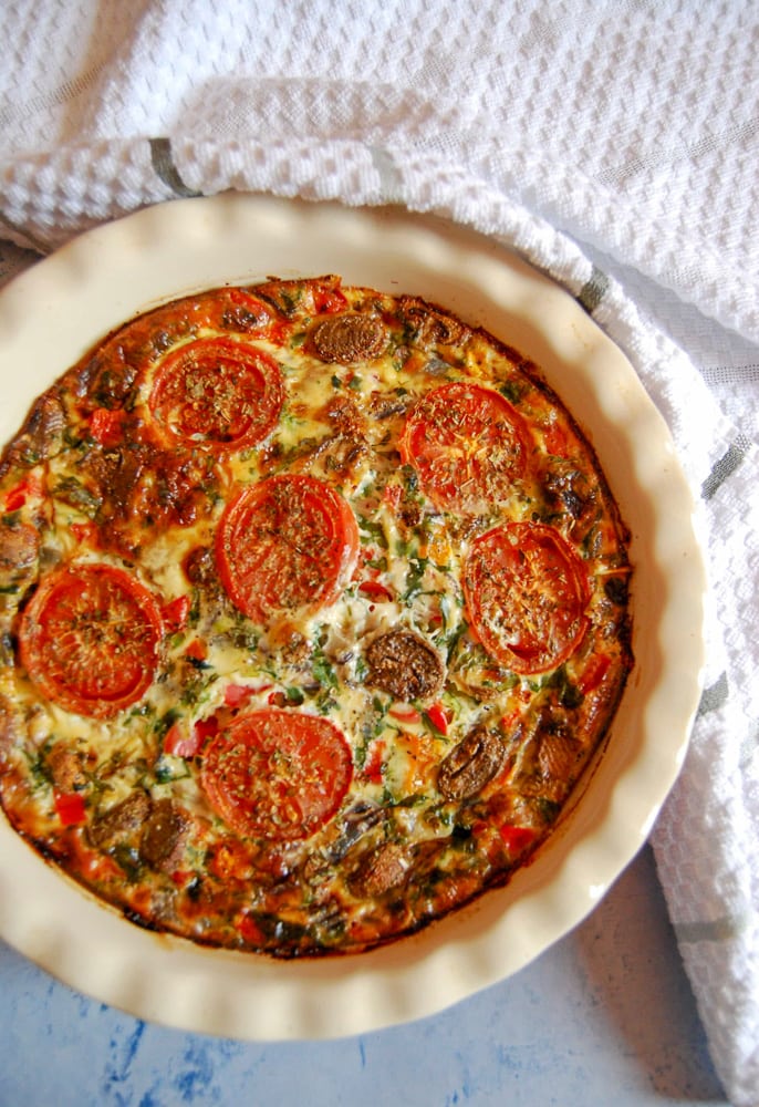 A Flat Lay photo of a crustless quiche with sliced tomatoes on top.