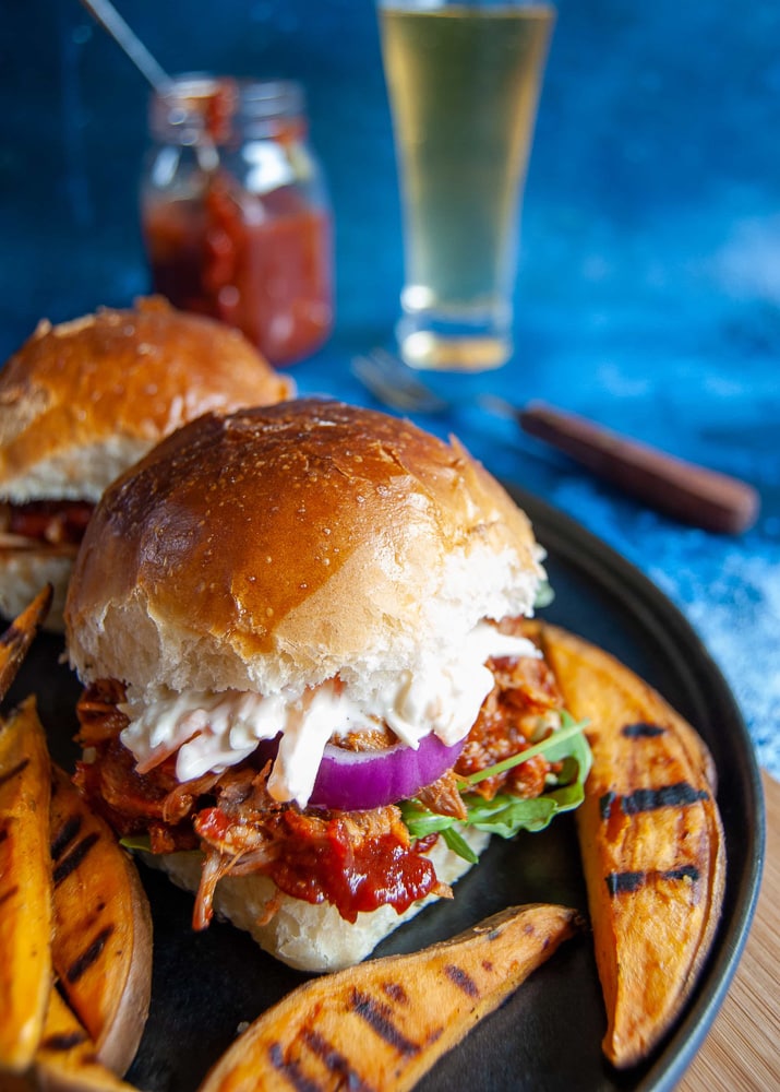 slow cooker pulled pork brioche burger with bbq sauce, red onion and coleslaw with sweet potato wedges on the side.