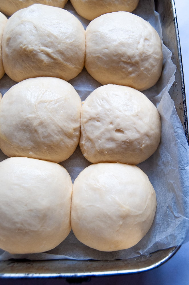 A batch of unbaked brioche buns in a lined roasting tin during their final rise.