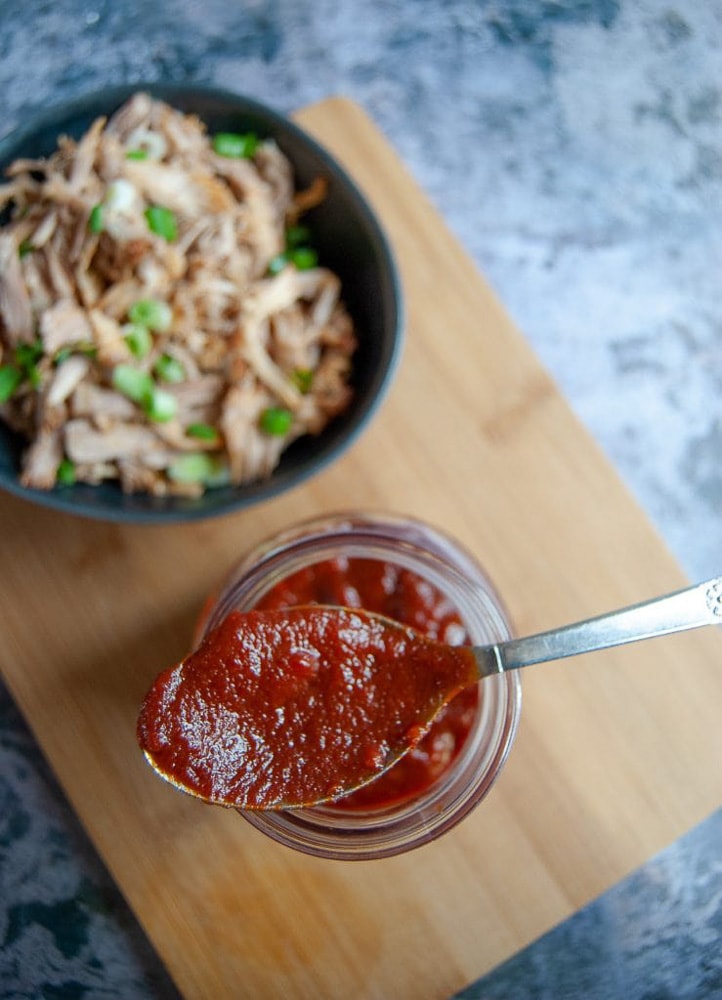 A flatlay picture of a jar of BBQ sauce with a bowl of slow cooker pulled pork on the side.