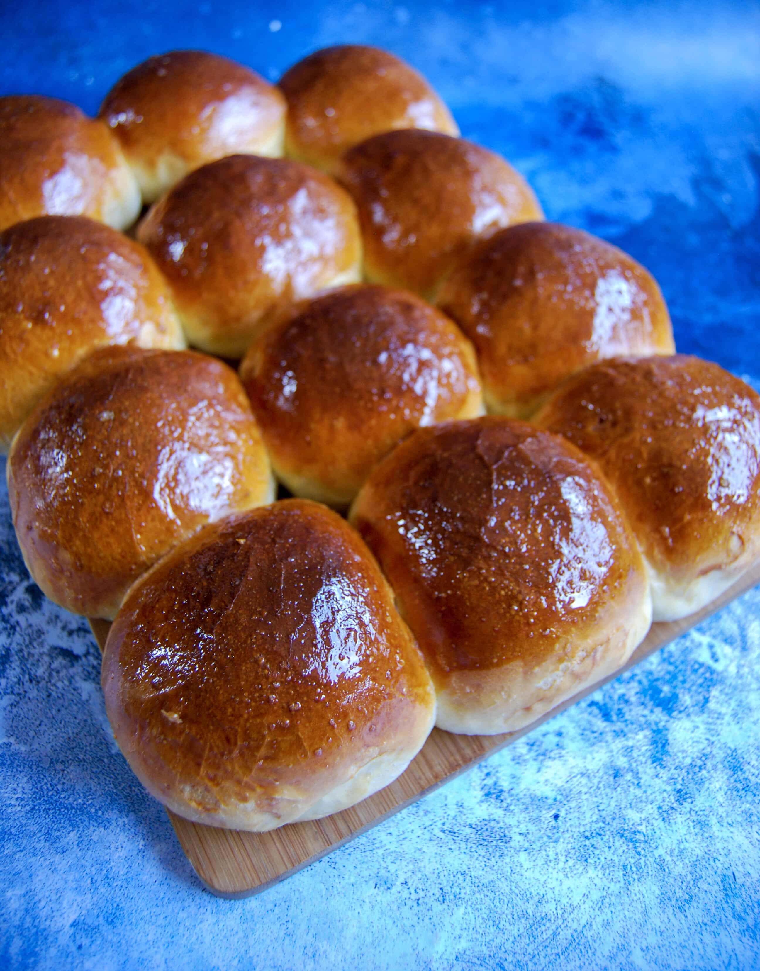 A batch of homemade brioche burger buns on a blue background.