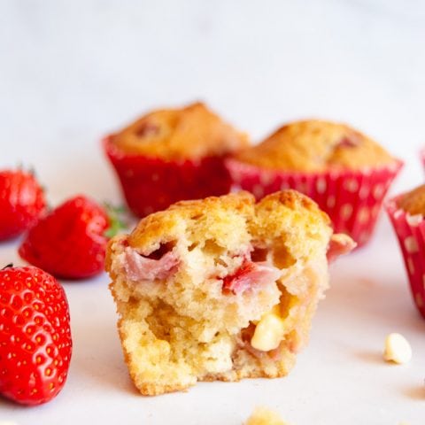 A halved strawberry and white chocolate muffin on a white marbled background. The muffin is filled with fresh strawberries and white chocolate chips.