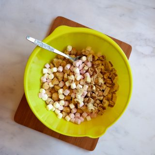 A yellow bowl of crushed shortbread, mini marshmallows and chopped up Twix bars for rocky road.