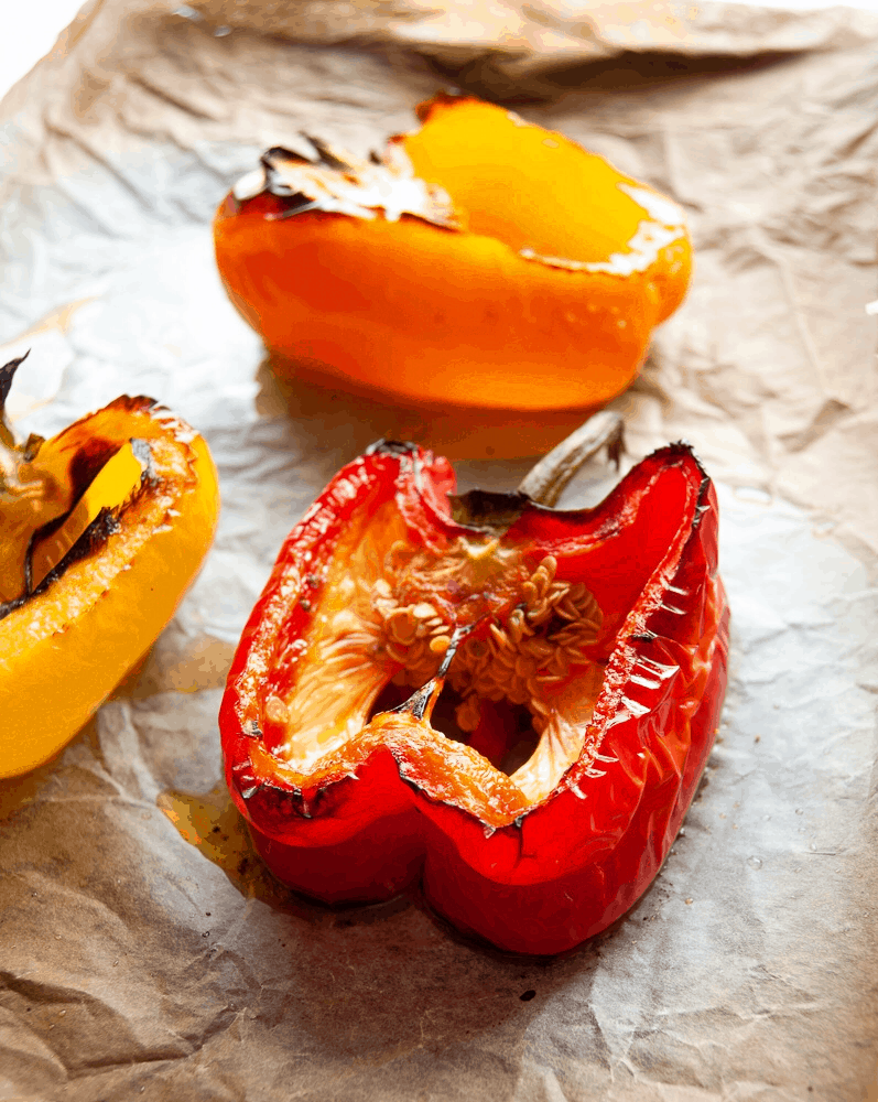 red, yellow and orange grilled halved peppers on a baking tray. 