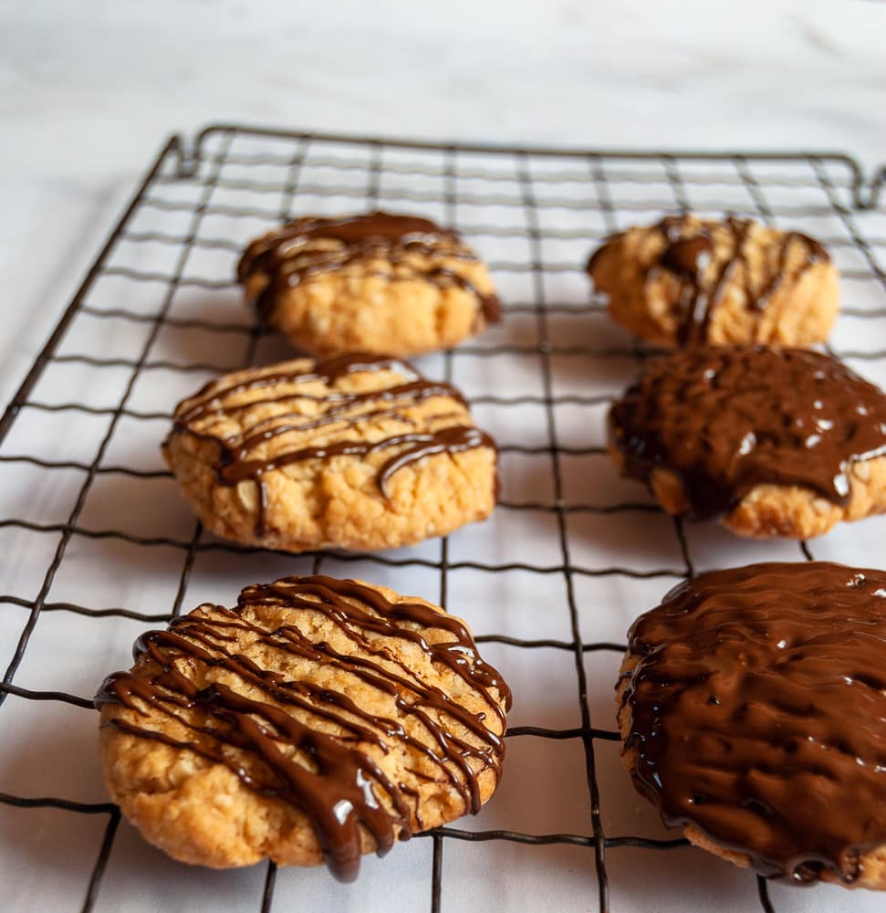 A close up picture of six oat biscuits drizzled with melted dark chocolate on a wire rack.