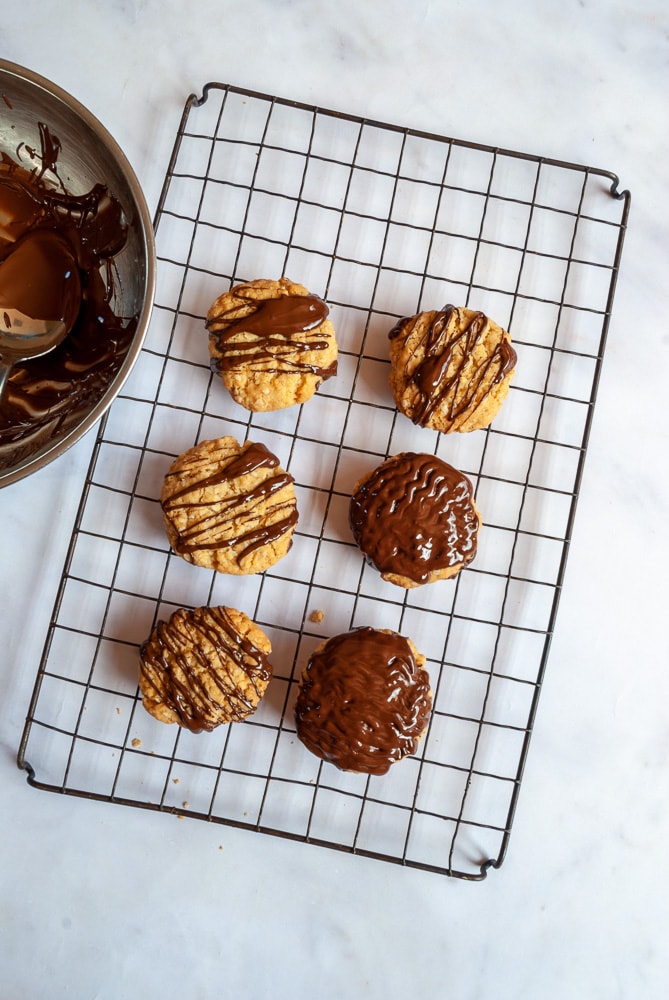 A flat lay photo of a wire rack with chocolate drizzled oat biscuits.