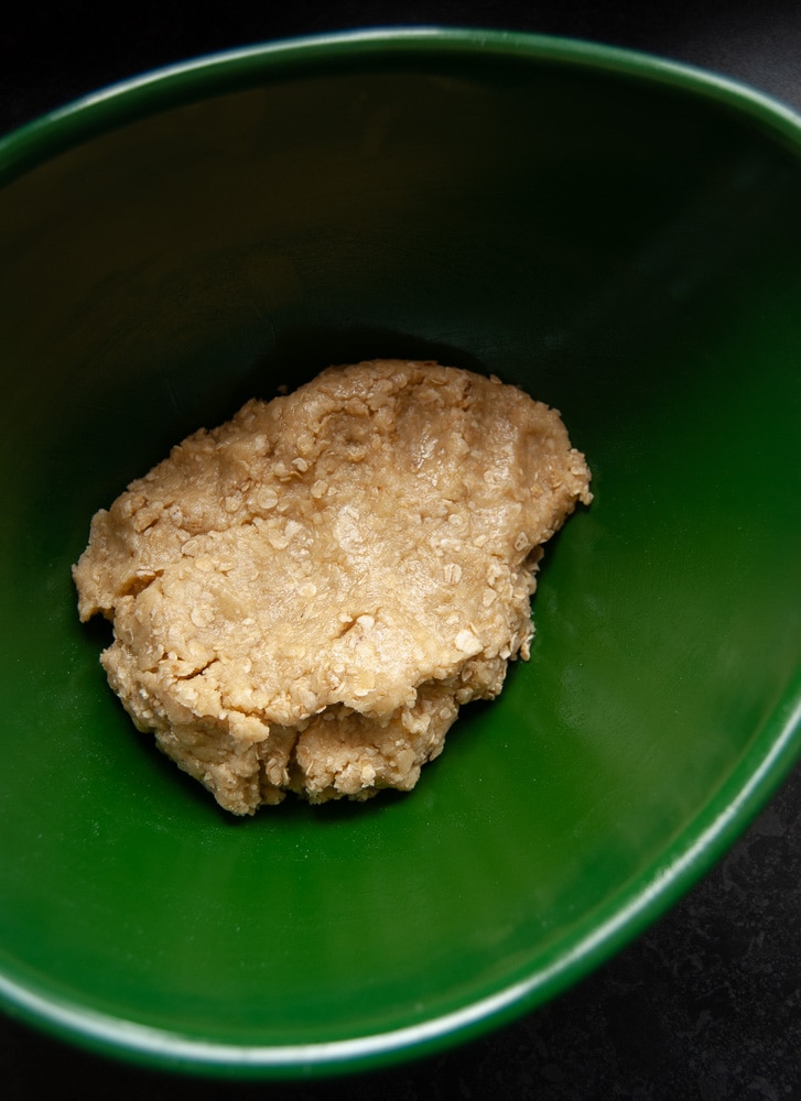 A green bowl of oat biscuit dough 