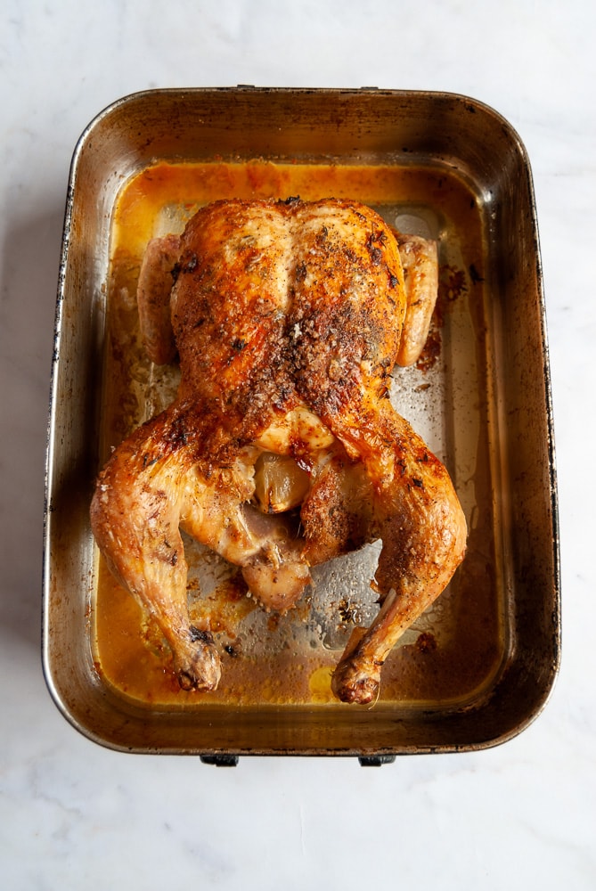 an image of a roasted chicken stuffed with a lemon in a roasting tin.