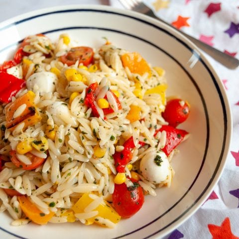 A bowl of Roasted Pepper Orzo Salad - Orzo salad with red, yellow and orange peppers, cherry tomatoes and mozarella pearls.