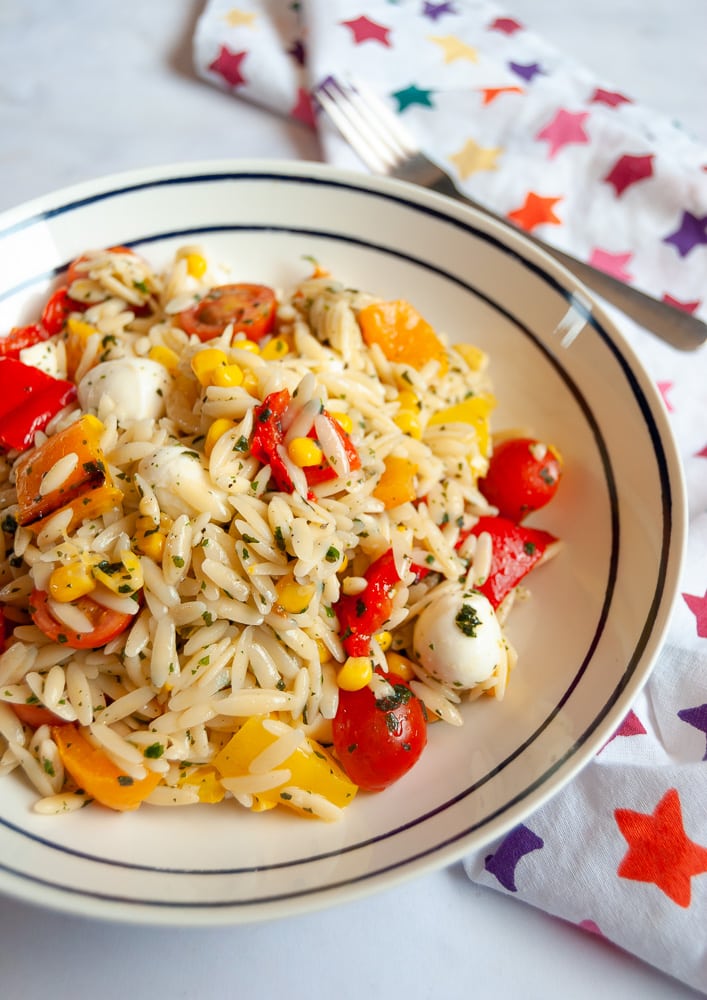 An Orzo salad with red, yellow and orange peppers, cherry tomatoes and mozarella pearls. 