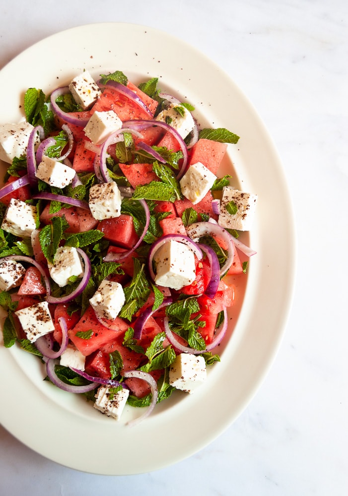 A salad with watermelon chunks, feta cheese cubes, fresh mint leaves and red onion slices sprinkled with Sumac.