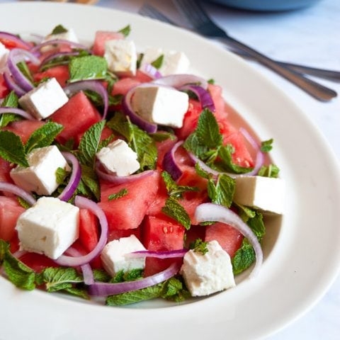 a watermelon salad with sliced red onion on a white plate.