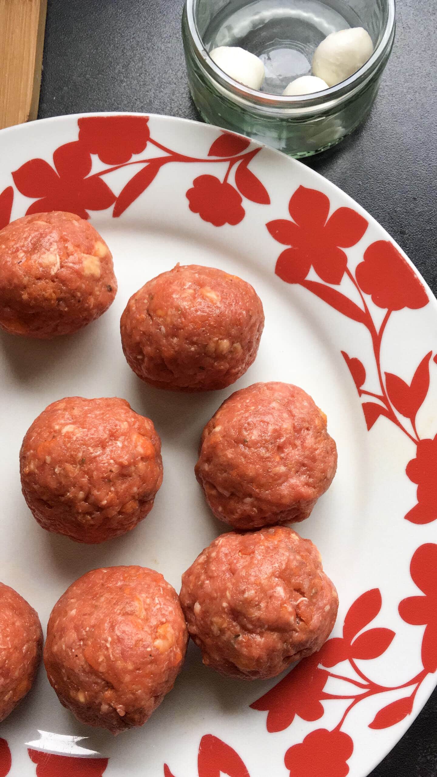 a red and white plate of unbaked beef meatballs