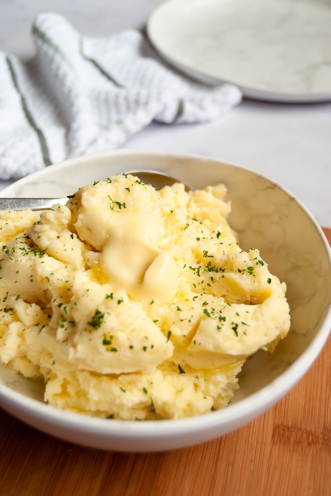 A bowl of creamy mashed potatoes with a pat of butter melting on top and a sprinkling of parsley