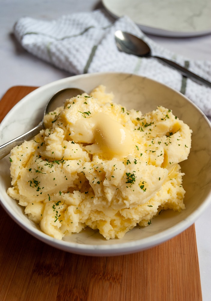 A bowl of creamy mashed potatoes with a pat of melted butter and spinkled with parsley