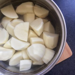 A saucepan of water and peeled and quarted potatoes for making mashed potatoes