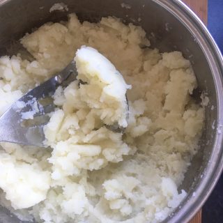 A pan of potatoes being mashed with a potato masher