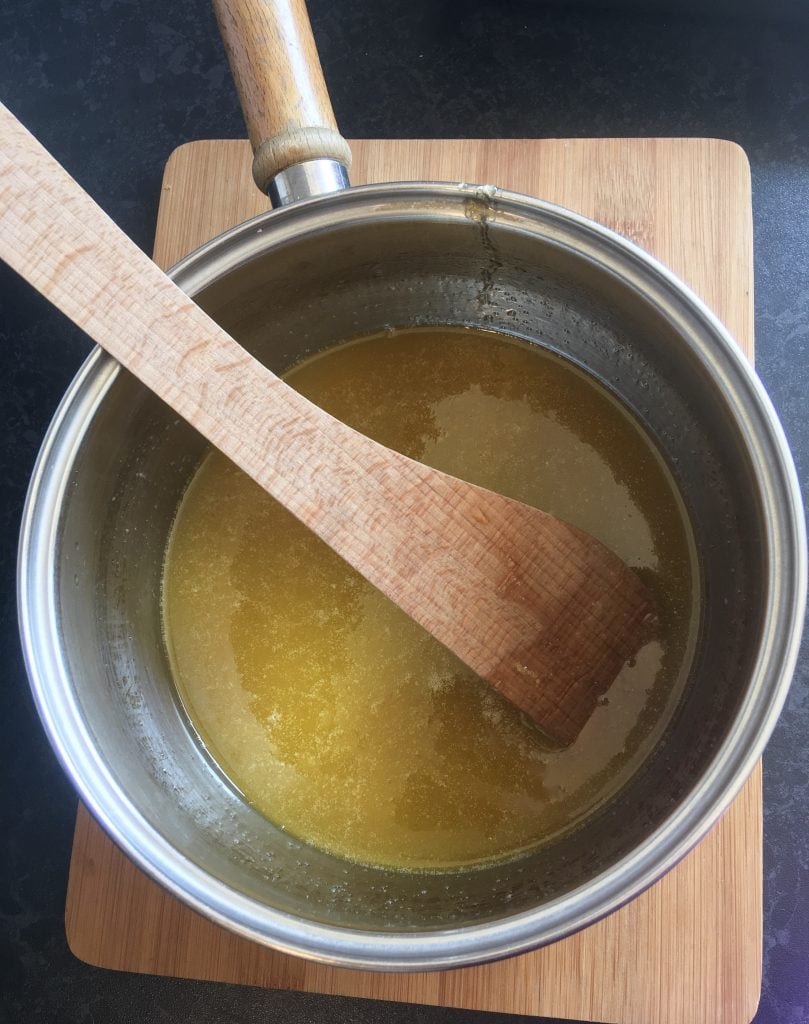 A pan of melted butter, sugar and syrup with a wooden spoon resting against the pan.