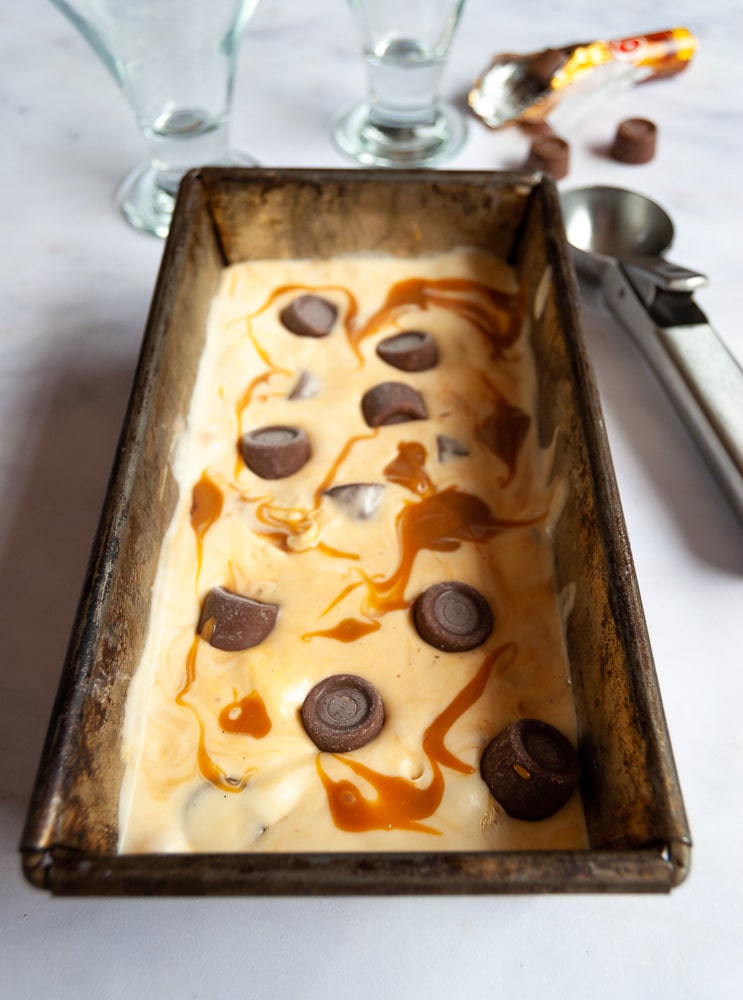 A loaf pan with no-churn salted caramel ice cream decorated with salted caramel swirls and rolos.