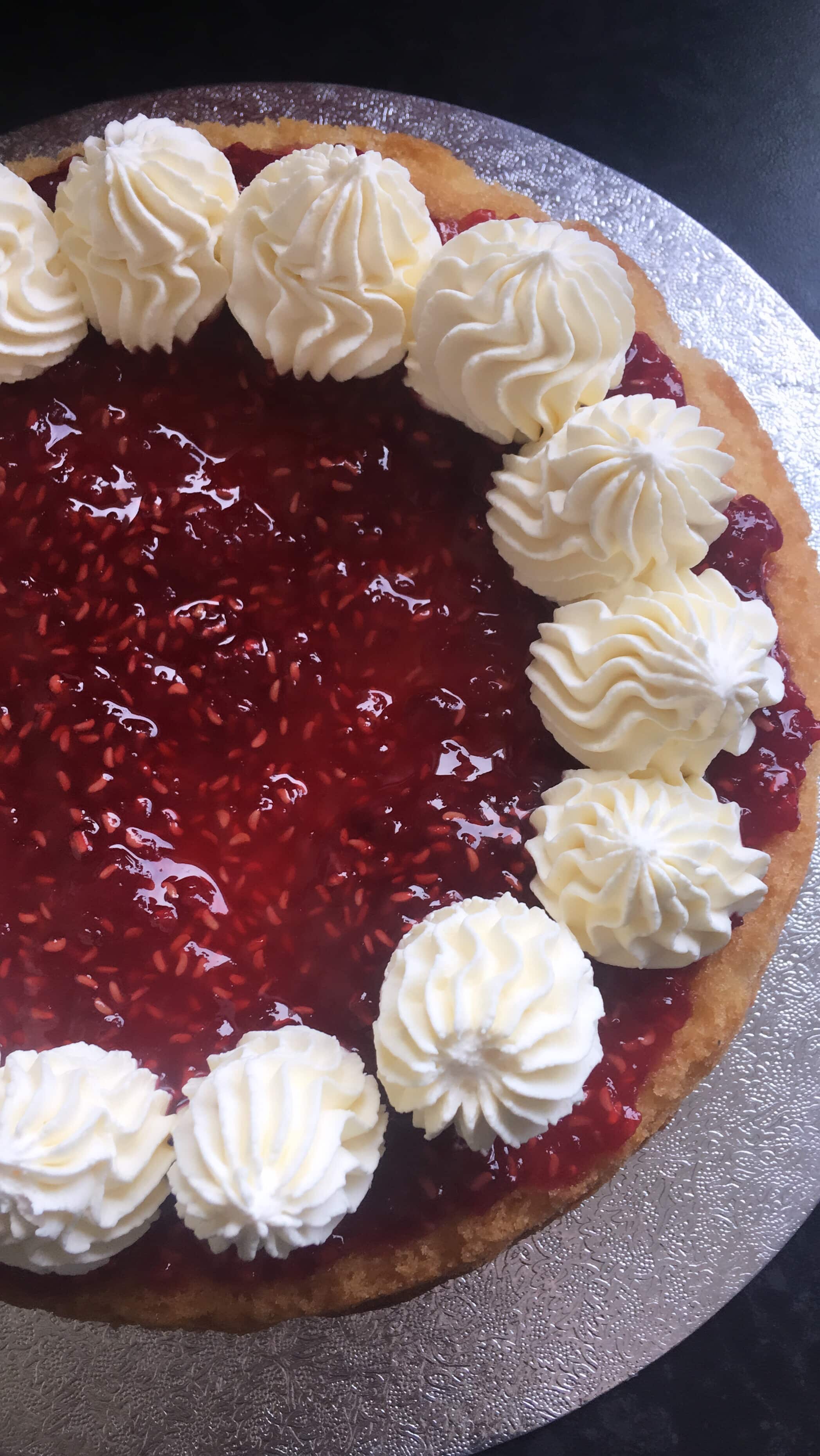 A photo of a sponge cake filled with raspberry jam and piped whipped cream