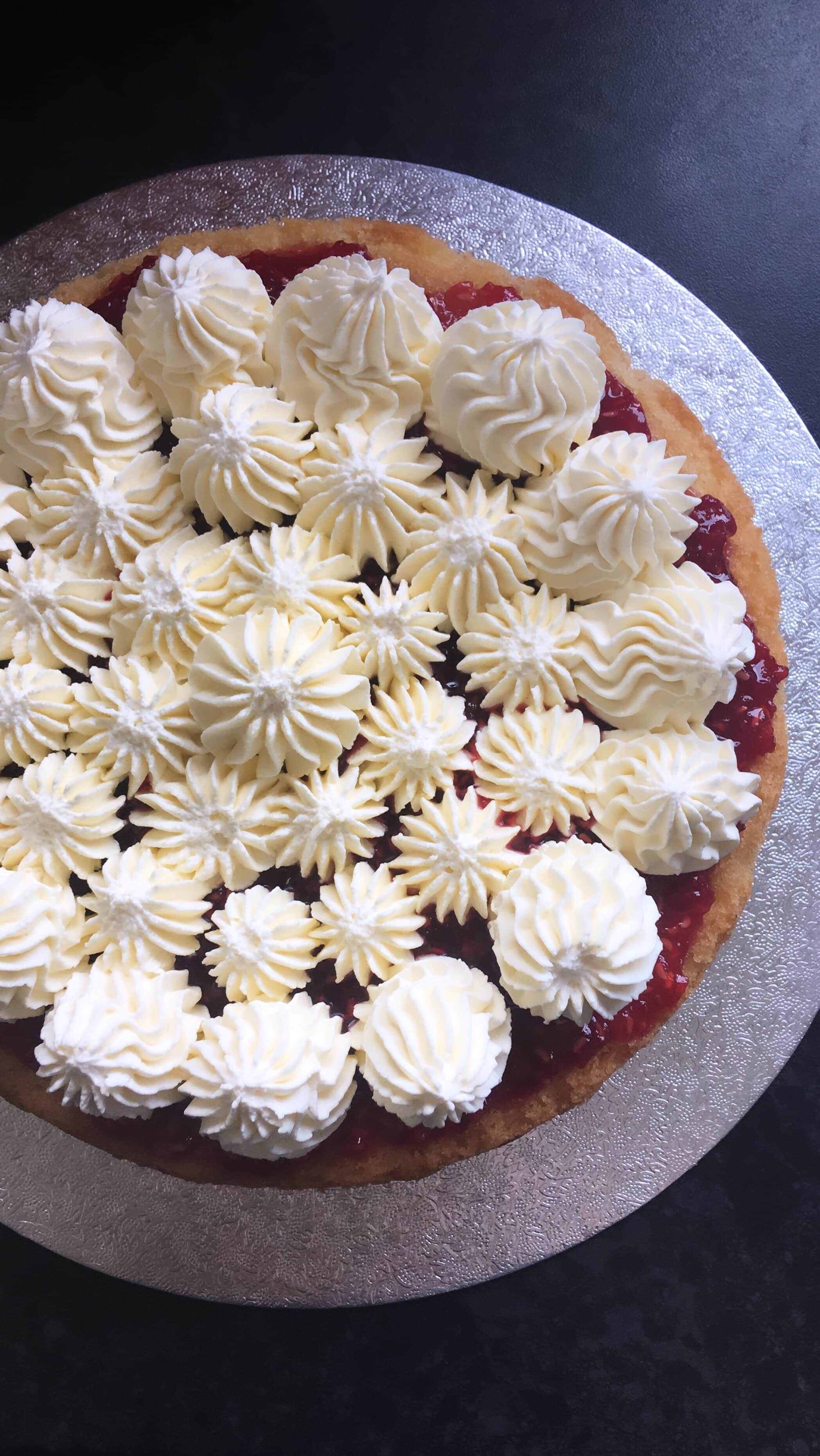 A close up photo of a sponge cake filled with raspberry jam and piped swirls of whipped cream