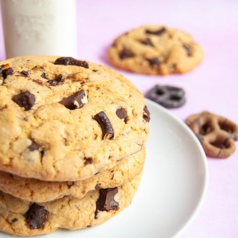 A white plate of chocolate pretzel cookies on a pink backdrop. A jug of milk and chocolate pretzels are also in the photo