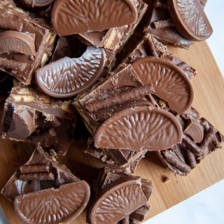 Pieces of no bake chocolate orange traybake with Matchmakers and Terry's chocolate orange segments on a wooden board.