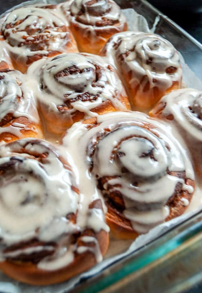 A freshly baked glass dish of cinnamon rolls with pumpkin puree covered in maple icing glaze.