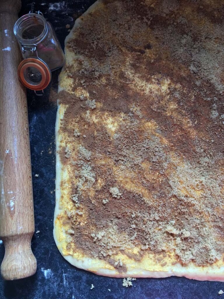 cinnamon sugar and pumpkin spice puree spread over a rolled out piece of bread dough and a rolling pin.