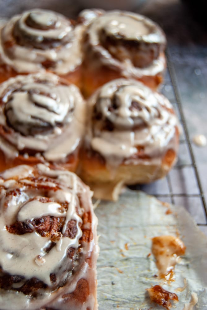 A close up photo of a batch of Cinnamon Rolls with a pumpkin puree filling and a maple syrup glaze on a wire rack