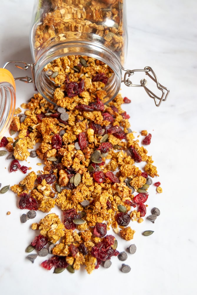 A spilled jar of Pumpkin spiced granola with cranberries and pumpkin seeds on a marbled white background