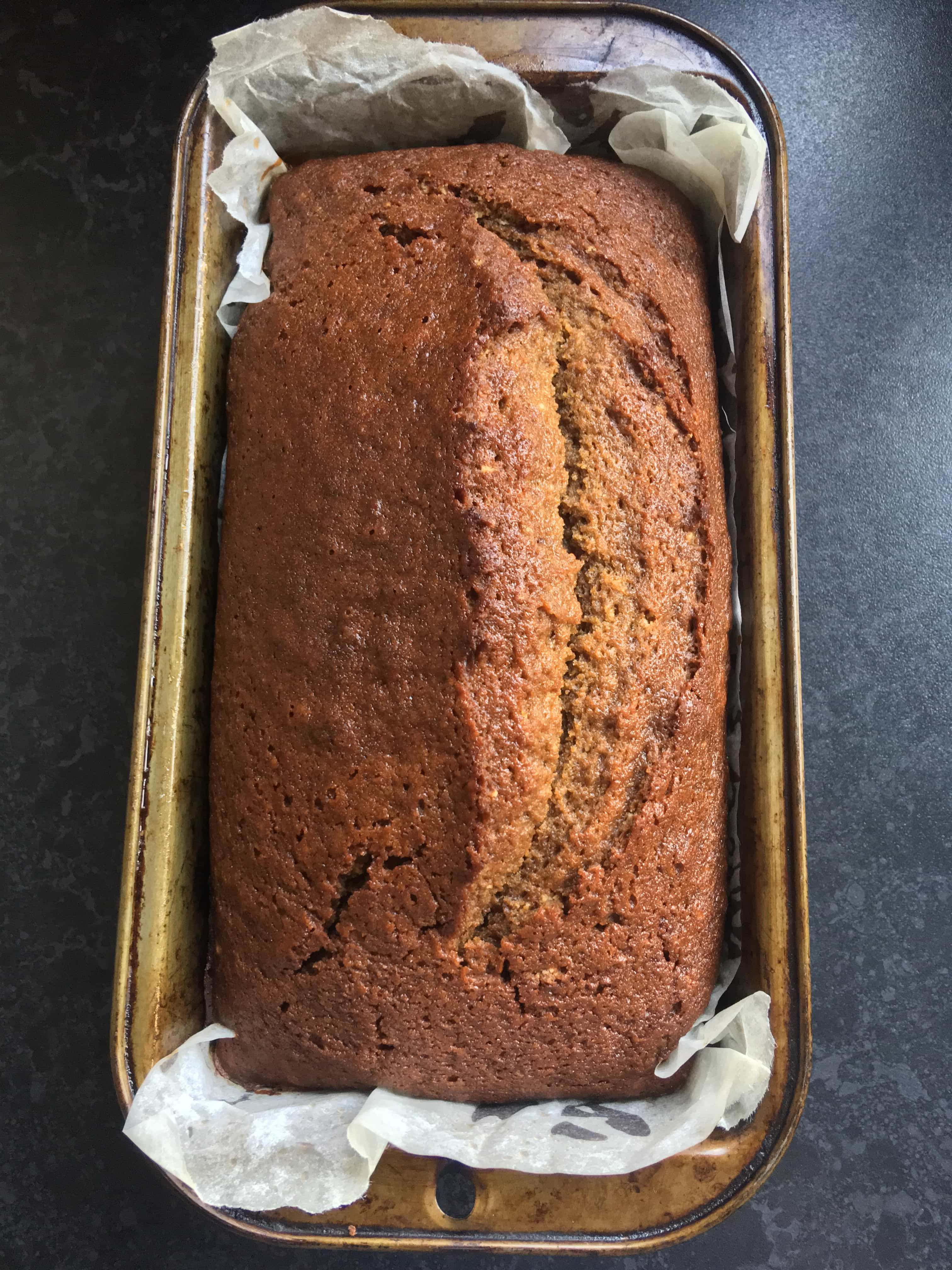 A freshly baked gingerbread loaf cake in a loaf tin on a dark background.