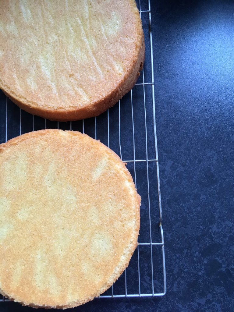 two freshly baked sponge cakes on a silver wire rack