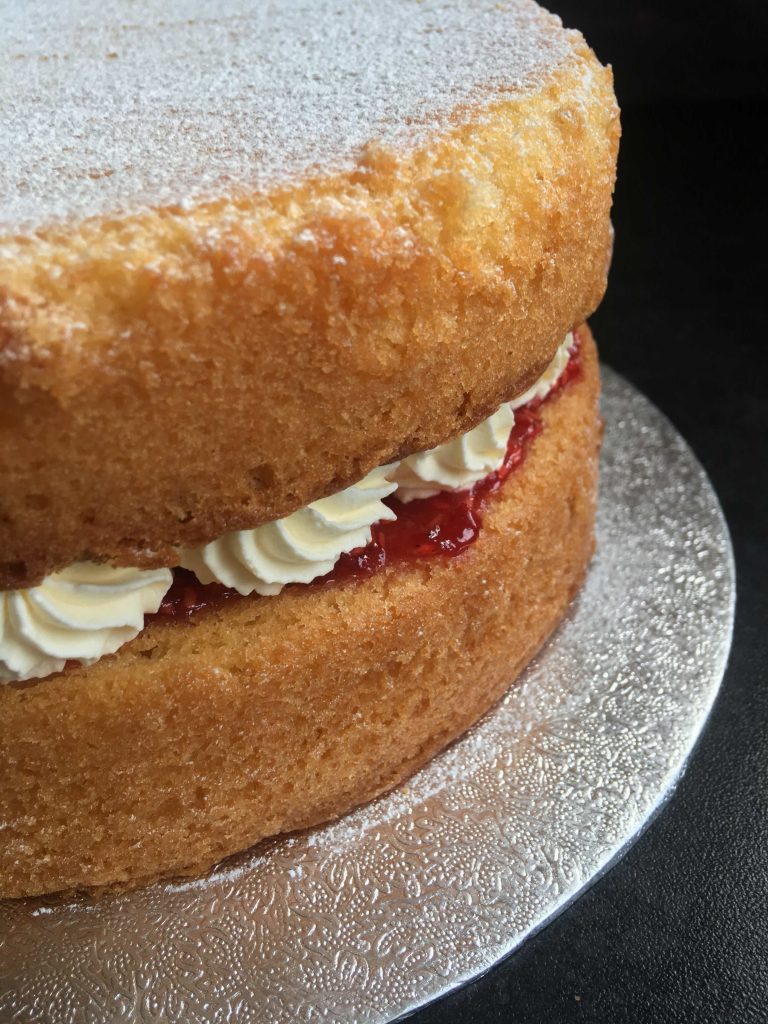 A close up photo of a sponge cake with jam and whipped cream