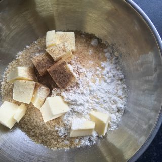 A silver bowl of cubed cold butter, flour, cinnamon and sugar for making a crumble topping.