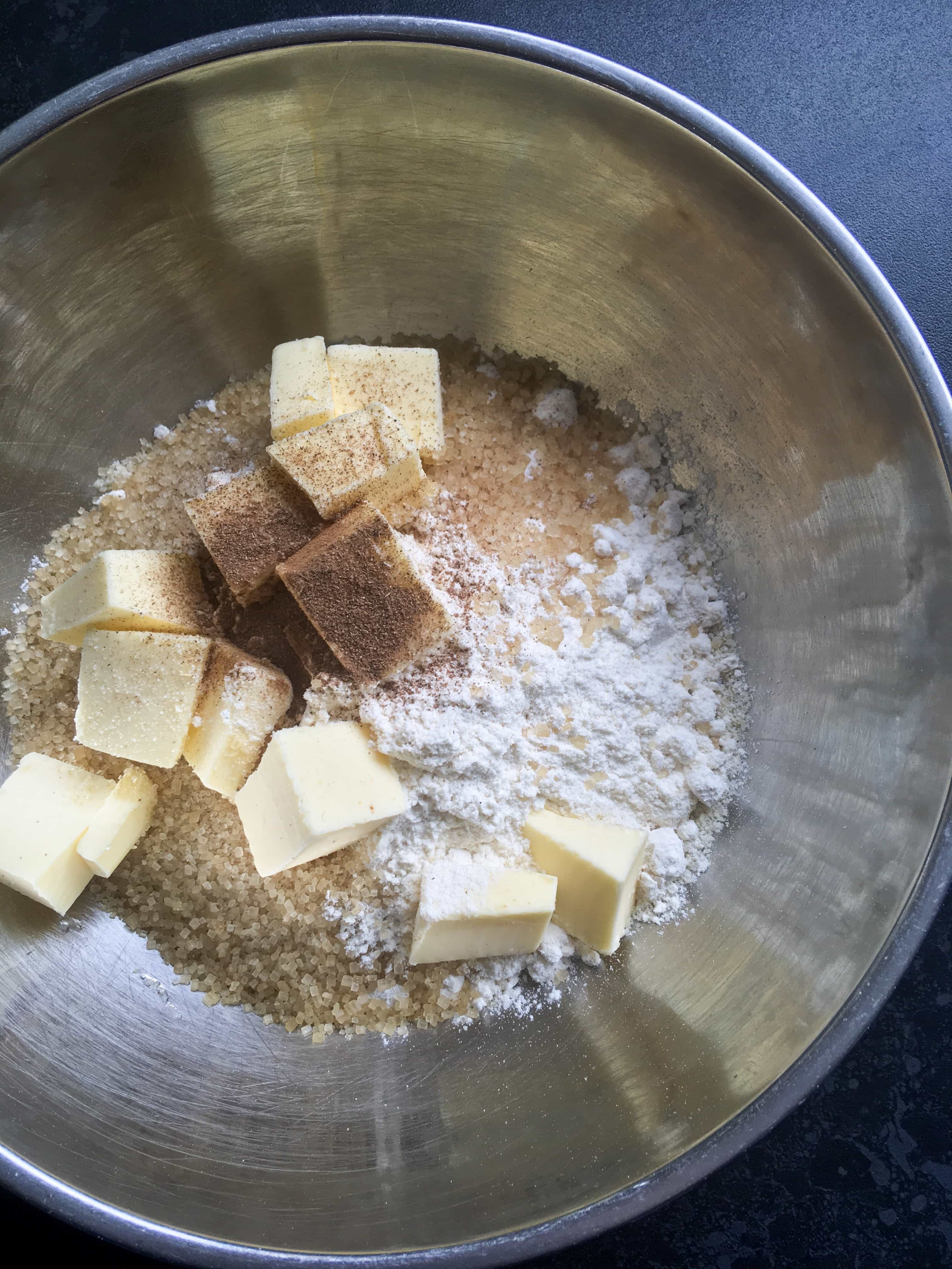 A silver bowl of cubed cold butter, flour, cinnamon and sugar for making a crumble topping.