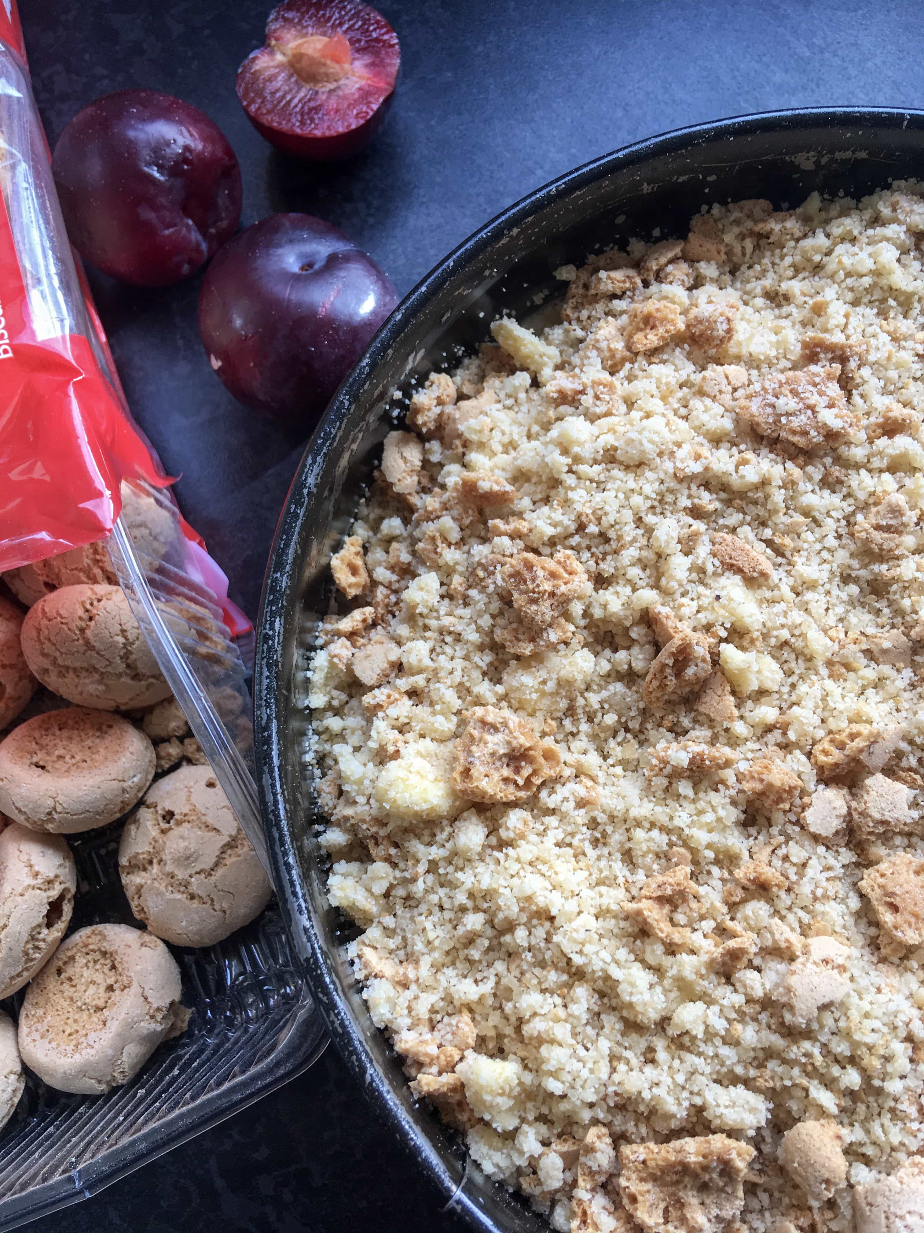 An unbaked Plum Amaretti Crumble Cake with a packet of Amaretti biscuits 