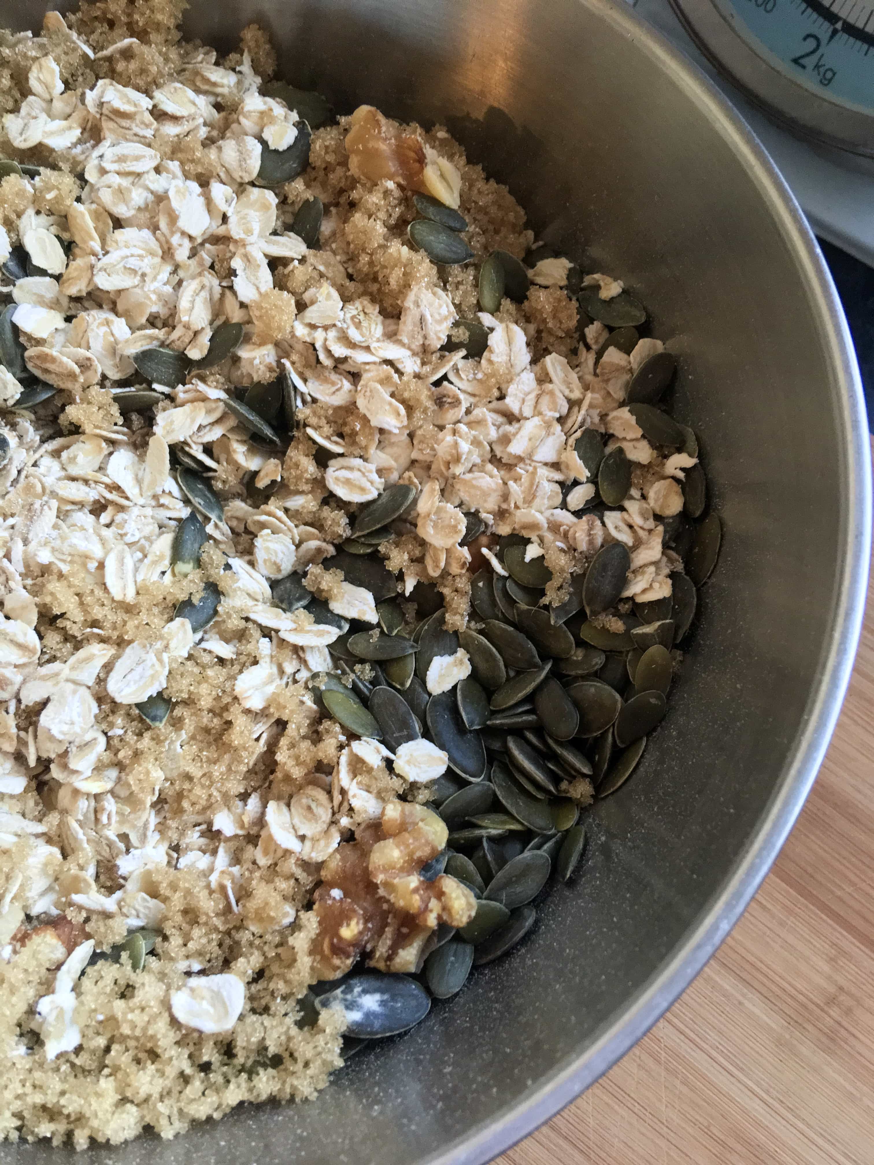 A silver bowl of oats, brown sugar and pumpkin seeds for making granola