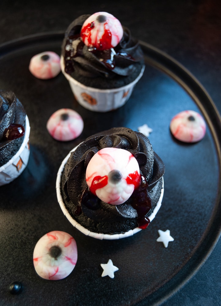 A flat lay photo of black velvet eyeball cupcakes on a black plate. 
