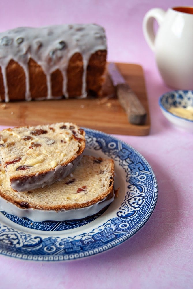 Slices of fruit loaf drizzled with an icing glaze on a willow pattern plate.