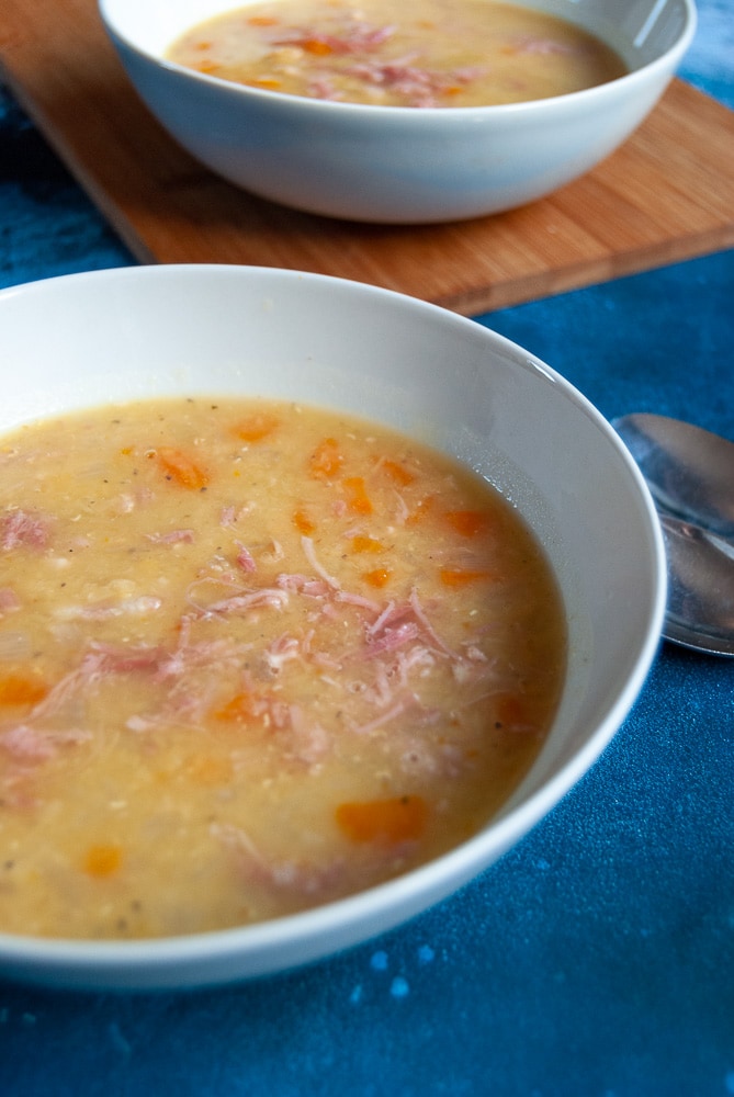 A white bowl of lentil and bacon soup on a dark blue background