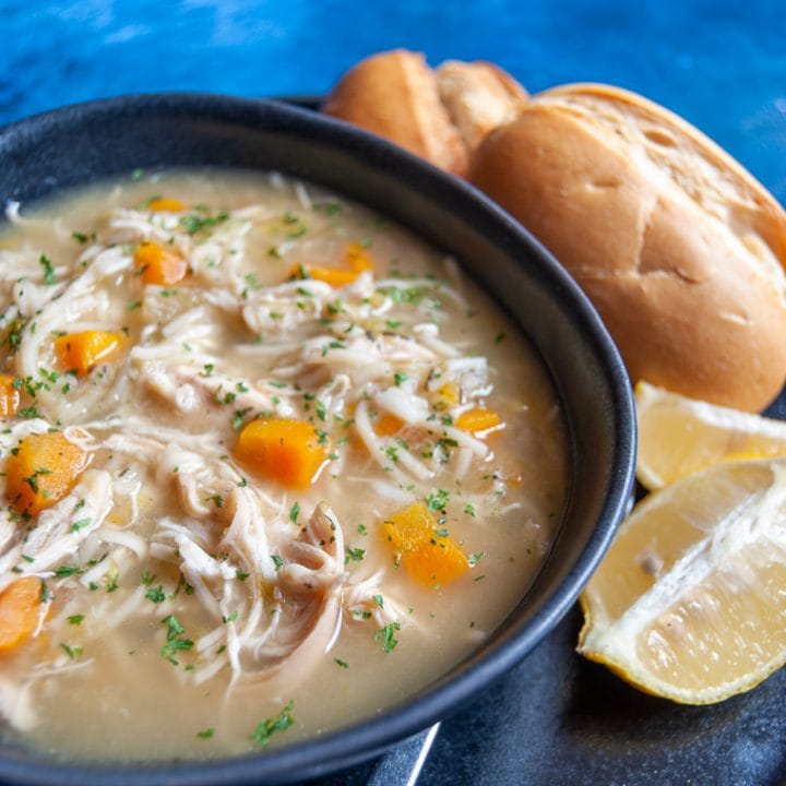 A bowl of chicken noodle soup with bread rolls and lemon wedges