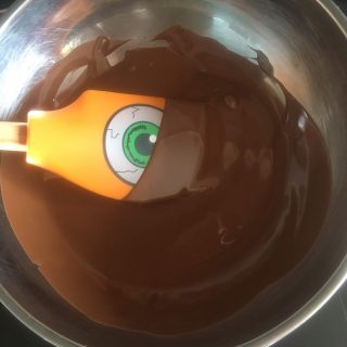 A bowl of melted chocolate and a Halloween orange spatula