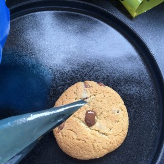 A chocolate chip cookie being decorated with melted chocolate