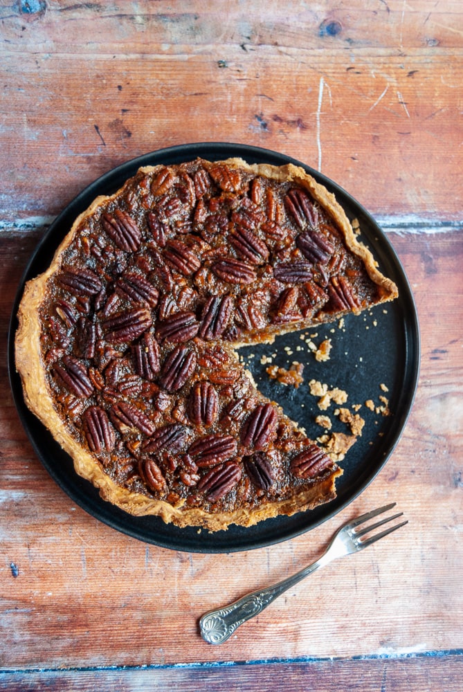 A Pecan pie on a black plate with a slice cut out of it. 