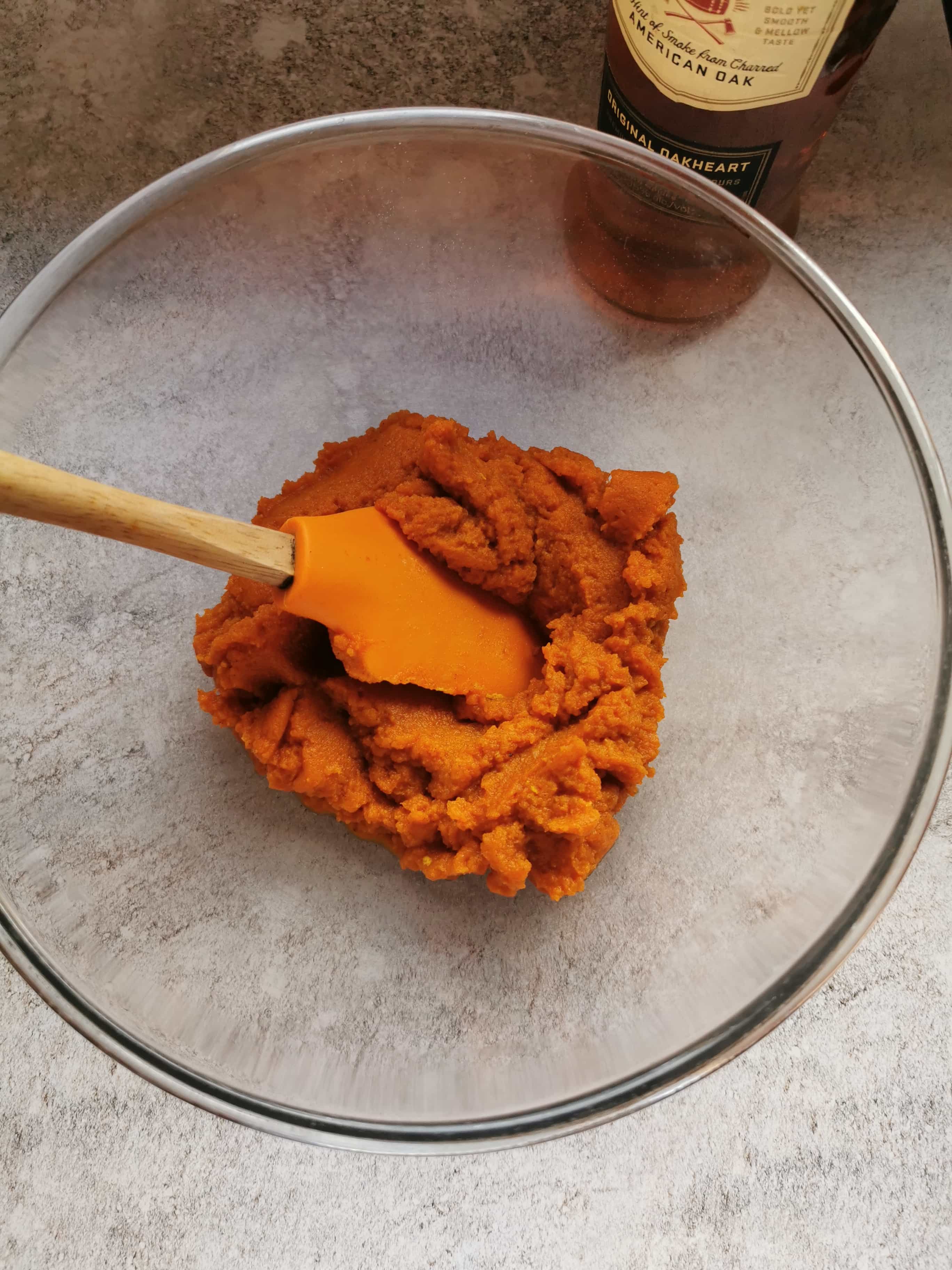 a pyrex mixing bowl of pumpkin puree with a wooden spatula.