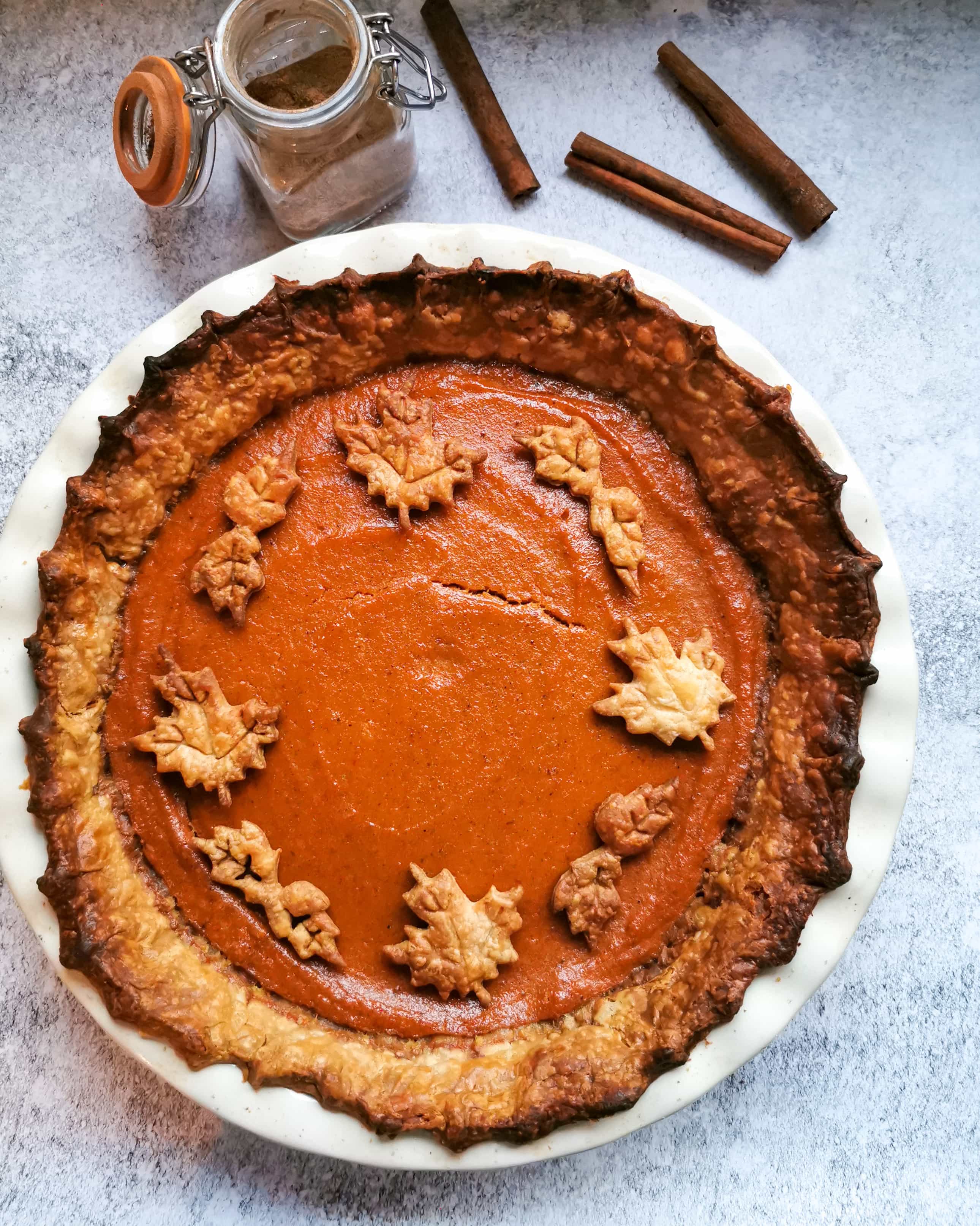 A pumpkin pie decorated with pastry leaves on a white and grey background
